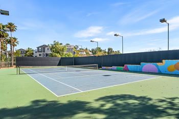 A tennis court with a blue surface and white lines, surrounded by a wall with colorful circles and a fence.